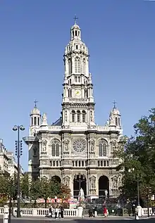 A 19th-century church in the French style, in light coloured stone, with a central tower with rounded top and smaller towers set back to left and right.