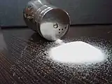 A small pile of white crystals in front of a tipped-over cylindrical with a few grains spilling out of the holes in its screw-top lid