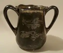 A tarnished, metal, double-handled cup. An inscription, in script, reads: "Univ of Penna/Relay Races/1895/Harvard vs. Pennsylvania."