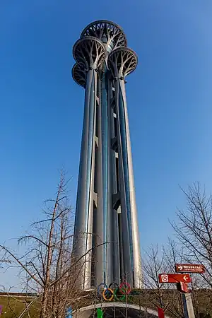 A narrow tower with several round, wider flat-roofed tops seen against a pale blue sky in winter