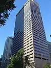 Ground-level view of a 40-story building with a white, concrete facade and dark windows; near the building's roofline, a prominent setback is visible