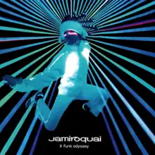 A man with a head-dress wearing a fuzzy jacket and sweatpants is leaping, green lasers appear to shoot from behind his head. The artist name and album title are displayed below