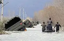 Albanian army rescuers and villagers pass by a convoy of trucks pushed to the side of the road by flood water on the outskirts of Bahcallek, near the city of Shkodra, Sunday, January 10, 2010.