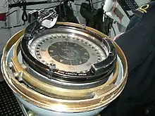 a colour photograph of a large compass surrounded by a brass ring installed on the bridge of a ship