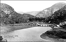 View of a river crossed by a wooden bridge, with brushy hills in the distance