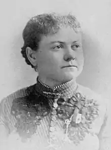 Portrait photograph of a middle-aged woman with her hair in an updo, and wearing a high-collared blouse.