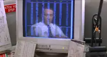 A computer monitor on a busy cubicle desk: The monitor displays a spreadsheet in seven columns which span the height of the screen. The monitor also shows the reflection of a middle-aged man in a shirt and tie, sitting close to the desk and wearing a telephone headset. The contrasts—the monitor's dark background, and the lightness of the text and the man's shirt—make the reflection more prominent between and behind the numbers.