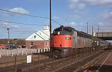 A passenger train with a streamlined diesel locomotive next to a modern brick station building