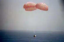 Spaceship descends over ocean with parachutes