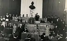 Charles de Gaulle speaking to a large group in a court-like room