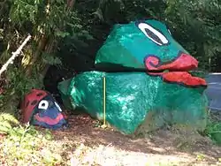 A pair of stacked rocks, painted green, with lips and eyes drawn on the top rock.