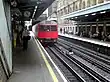 A red train with a grey top and a black sign that reads "CIRCLE LINE" in yellow letters is on railway tracks leading from the background to the foreground.