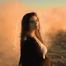 Photo of the artist stood in a desert with a sand cloud floating behind her.