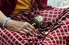 Lap of woman in red and white kira dress with a pattern that features X-shaped details where the white stripes meet; prayer beads are also featured in the photo