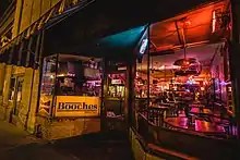 Front door and windows of the venue at night after closing time, with a black-and-white 'Booches' sign, and a view of the tables and bar inside.