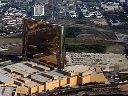 A tall, reflective, bronze-colored hotel tower sits atop a smaller structure, next to a parking garage.  A highway and city streets are visible in the background.