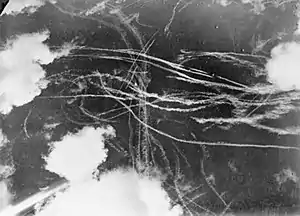 A picture of a piece of sky with several clouds and many condensation trails caused by many aircraft. Each trail curves around the other indicated an air battle