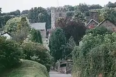 Several buildings including a square church tower amongst trees.