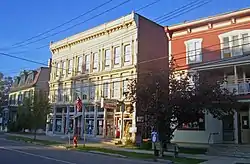 Three buildings in a row lit by late afternoon sun and partly in shade. The left one is green and red, the middle one cream-colored and the right one reddish-orange