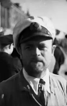 A bearded man wearing a white peaked cap, and an Iron Cross displayed at the front of his uniform collar.