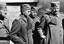 A black and white photograph of four older males in military uniform wearing peakless caps