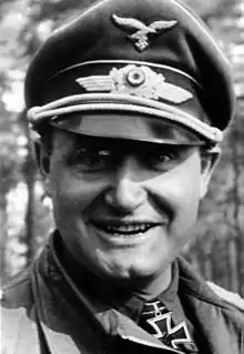 A man wearing a military uniform, peaked cap, and an Iron Cross displayed at the front of his uniform collar.