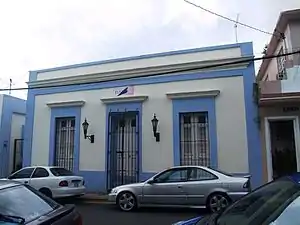 Photograph of the Stahl House, a one-story, rectangular facade with a flat roof, central doorway bay, bays flanking the doorway with louvered shutters, and bars over all three bays