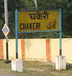 Yellow ailway location sign with english and Indian town name written in black lettering