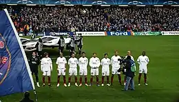 group of several men in several rows, standing, dressed in black and white football kit, flanked by man with camera