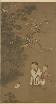 Two young girls play with a toy consisting of a long feather attached to a stick, while a cat watches them. There is a large rock formation and a flowering tree to the left of the girls and the cat.