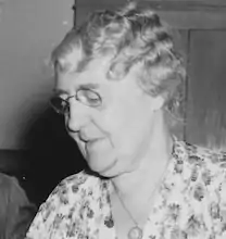 small headshot of an older white woman with curly grey hair looking down and to the left