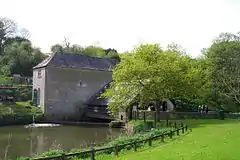 Gray stone building with slate roof. Attached to the right is a wooden structure over water, partially obscured by trees