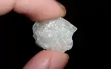 A shiny translucent white crystal of methamphetamine, held between the ends of a finger and thumb