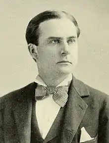 A man with black hair wearing a black jacket and vest, patterned bowtie and white shirt and pocket square