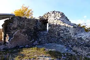 Walls forming an angle. In the middle of the one on the right is a small opening. On the left wall, part of the original plaster remains.