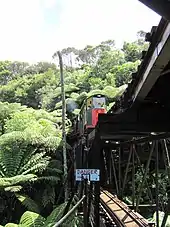 A bi-level railway bridge carries a small passenger train on the upper level. The lower level is marked with a "Danger" sign.