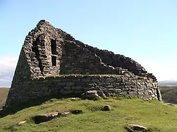  The ruins of a double-walled circular stone tower on top of a green hillock with a blue sky in the background