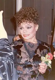 A photograph of a woman in a black dress holding a red flower. She is looking away from the camera.