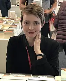 Mandel smiling, seated at a table with books