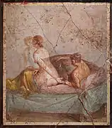 A nude woman, getting up towards the foot of a bed, reaches back towards her male lover, lying down in it.