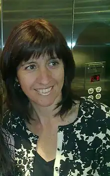 Smiling woman with brown hair, wearing a black blouse and a black and white sweater.