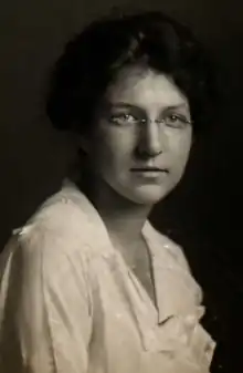 A young white woman with dark hair, wearing eyeglasses and a white blouse