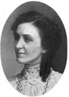 A white woman with dark hair, seen in 3/4 profile; she is wearing a high lace collar and a chain necklace.