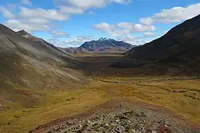 Wide treeless valley between sloping mountains with a snow-capped mountain in the background