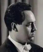 Clean-shaven man with oiled and brushed-back hair, in formal dress