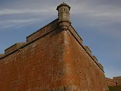 Corner of an old fortress with orange lichen-covered walls under a clear sky.