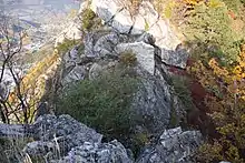 Hole between two rocks. A stone wall is built on the farthest rock and there are bushes between the two rocks.