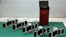 Small PicoSatellites lined up on a white table in a lab.