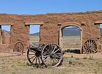 Old wagon wheels in front of a ruined clay wall with arched opening and windows