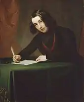 A man with shoulder-length black hair, sitting at a desk, writing with a quill